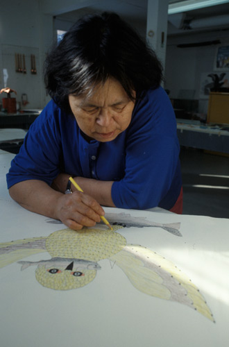 Qaunak Mikkigak using coloured pencils to draw a snowy owl with a fish in its beak and a second fish in its talons