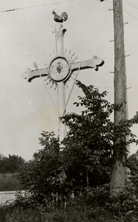 Wayside cross with fleur-de-lis endpoints, adorned with a sun and a heart at its axis, a rooster on top and other devices. Saults-aux-Rcollets, Qubec, [191-]., © CMC/MCC, Edouard Zotique Massicotte, B557-6.27