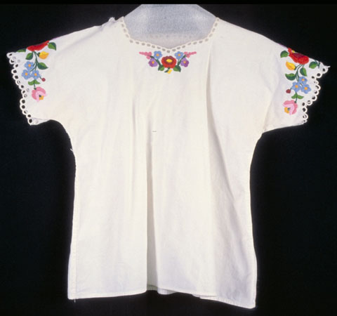 Female's short-sleeved, white cotton blouse with multi-coloured embroidered floral motif and around the sleeves and front. This is part of a traditional costume., © CMC/MCC, 76-514.1