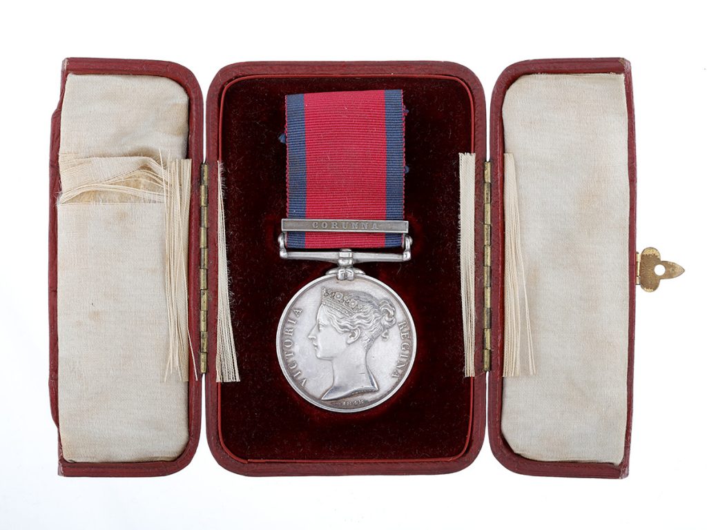 A silver military medal with a blue and red ribbon, displayed in a brown box with a black and white lining