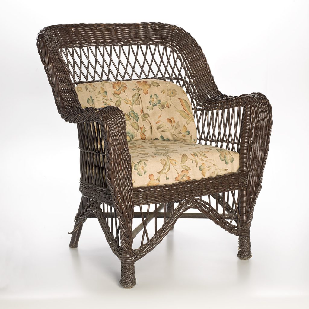 A woven wicker armchair with cream coloured floral seat cushions