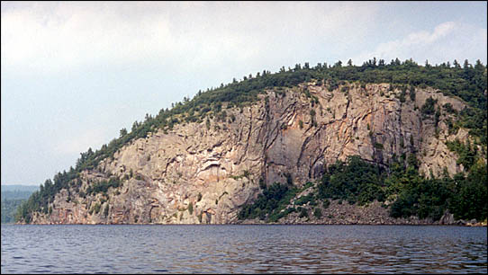 A landscape of a big stone cliff at the edge of a lake.