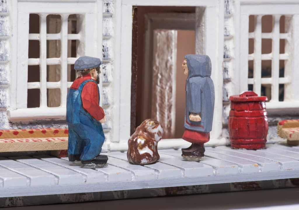 Gros plan du balcon d’une maison où l’on peut voir deux villageois en miniature. Le chat en céramique constituait un cadeau à l’achat d’une boîte de thé Red Rose. Musée canadien de l’histoire, IMG2015-0289-0007-Dm