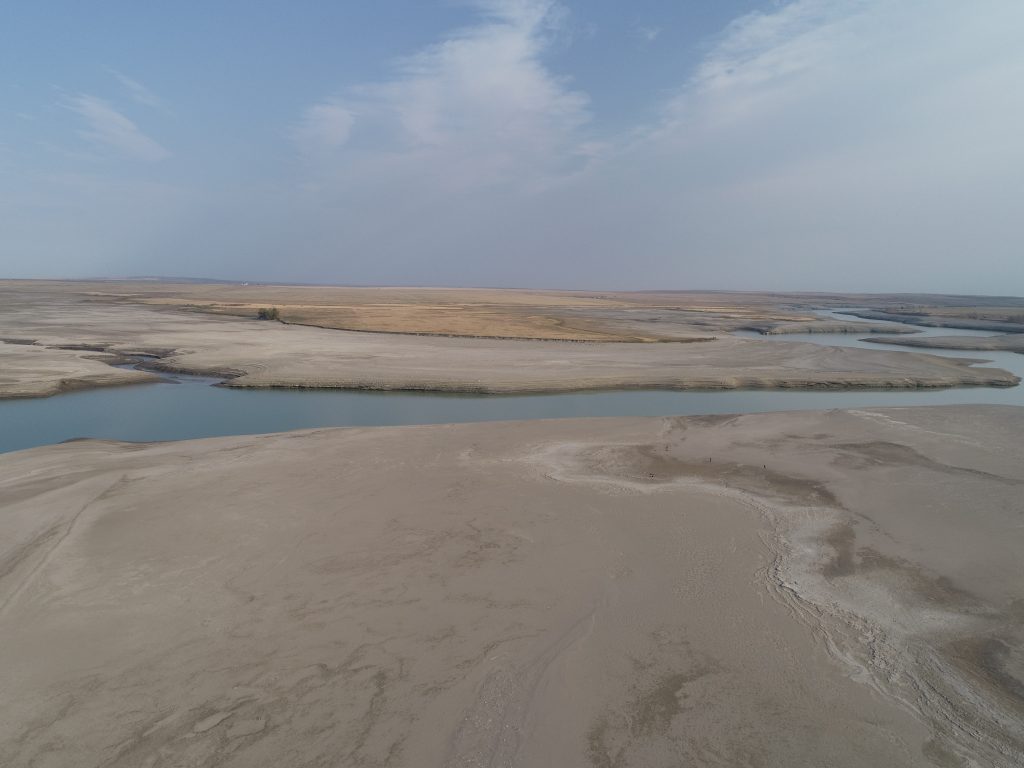 A north-facing aerial view of Wally’s Beach and the St. Mary Reservoir at low water, showing the original channel of the St. Mary River. Across the river lies Kainai Nation land.