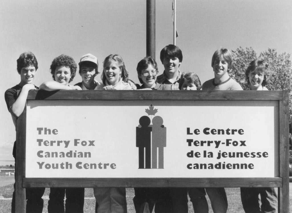 Nine smiling teenagers stand behind a sign reading “The Terry Fox Canadian Youth Centre.”
