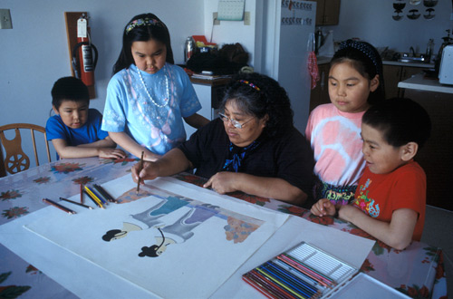 Pitaloosie Saila, surrounded by children, using coloured pencils to draw what would become a print depicting two women