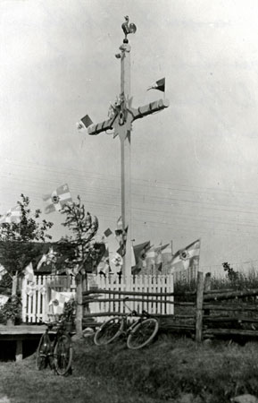 Croix de chemin ornementée d'un soleil à l'axe et d'un coq à la cime et agrémentée de drapeaux papal. Saint-François, Québec, 1923., © MCC/CMC, Edouard Zotique Massicotte, 60026