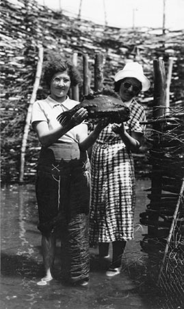 Deux femmes tenant une poule de mer (lompe) devant un enclos à l'Île de la Providence, Québec, 1937., © MCC/CMC, Marius Barbeau, B314-17.3