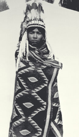 Young Nlaka'pamux (Thompson) man wearing an eagle feather bonnet and a woven goat hair blanket wrapped around his body, British Columbia, © CMC/MCC, J.A. Teit, 30991