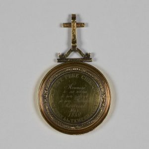 Circular medallion with engravings and a cross on top.