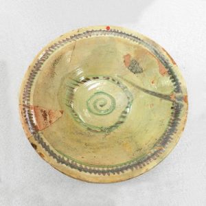 Cracked ceramic plate with a pale green glaze and purple and green designs