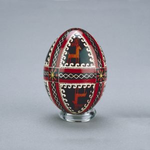 A Ukrainian Easter egg decorated with mirror images of deer, divided by intricate spiral and ribbon shapes, intersected by flowers.