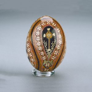 A Ukrainian Easter egg decorated with an intricate diamond pattern in red, black, brown and orange around a central cross.