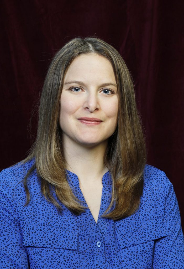 Headshot of a woman smiling in a blue button-up shirt.
