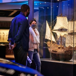Two people engage in front of a display case containing a model of an old ship
