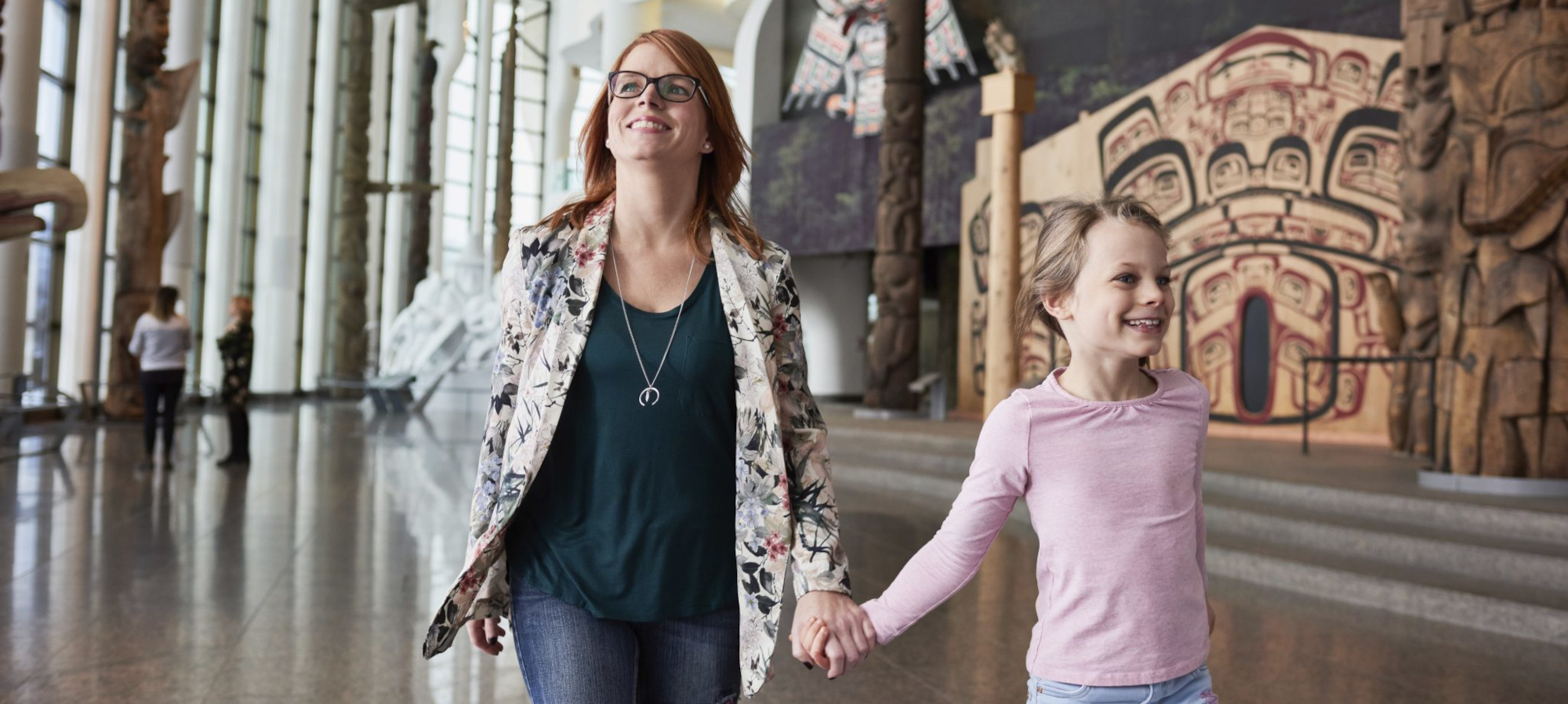 A woman and a child walk hand in hand through the Canadian Museum of History in Ottawa, surrounded by various artworks and exhibits on display.