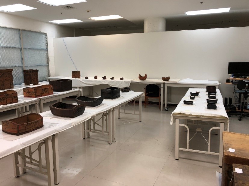 A room with white walls and several long tables, covered with dozens of wooden items in various sizes.