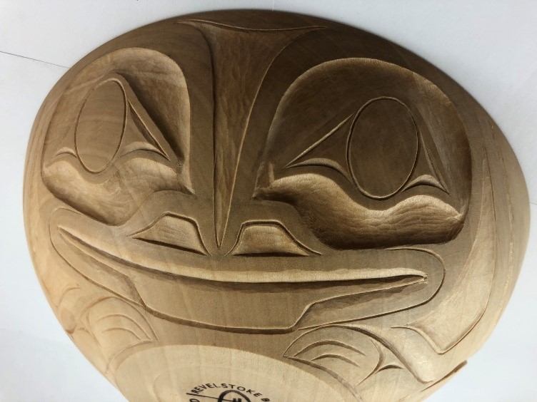 A large wooden bowl with a stylized frog’s face carved into the outside.