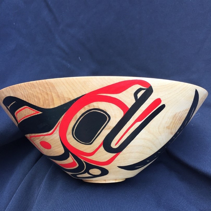 A large wooden bowl painted with a stylized orca in black and red.