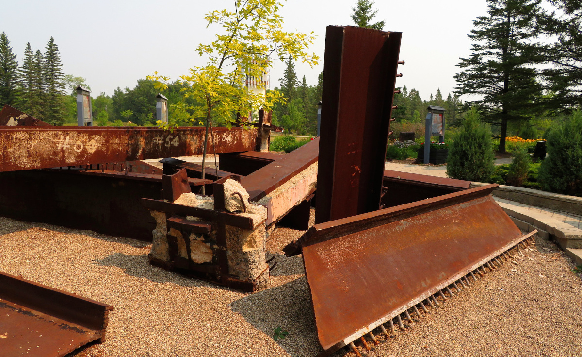 A large sculpture made of huge rusty I-beams and concrete, placed as though fallen.