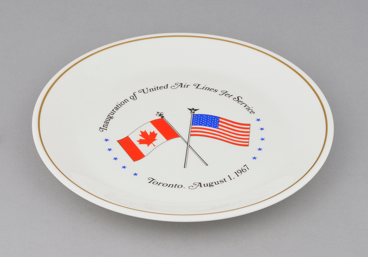 White ceramic plate with crossed Canadian and U.S. flags, encircled by the words, “Integration of United Air Lines for Service, Toronto, August 1, 1967.”