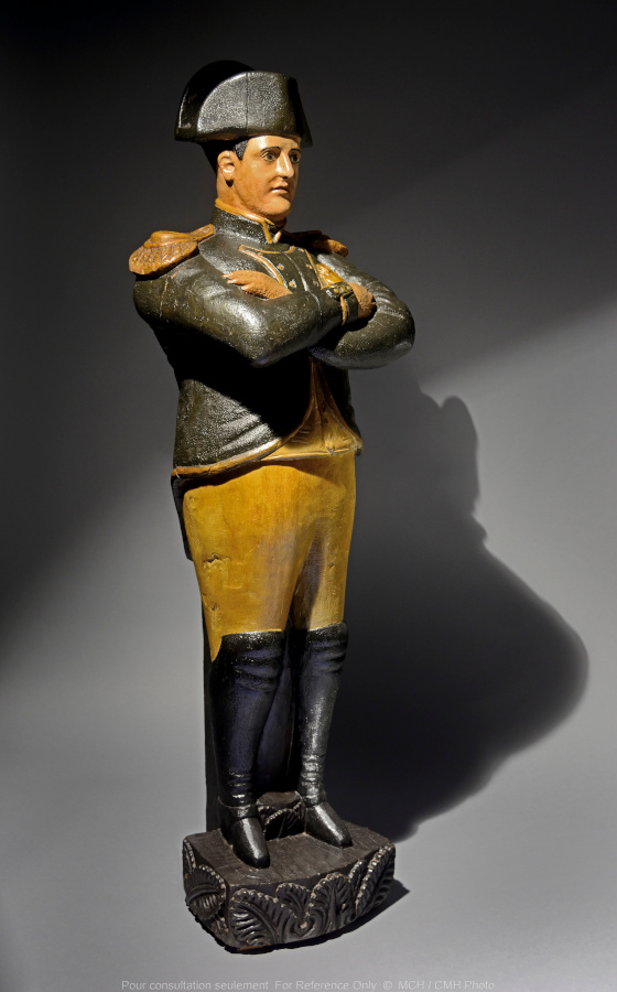 A statue of a man wearing a large hat and high boots, standing with his arms crossed.