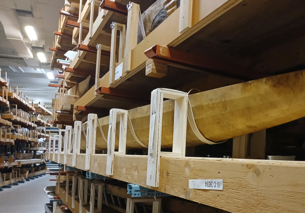 A series of fabric straps attached to plywood supports cradle a kayak on a storage shelf.