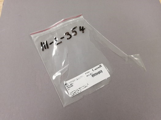 A torn Ziploc-style plastic bag with a computer-printed and handwritten labels.