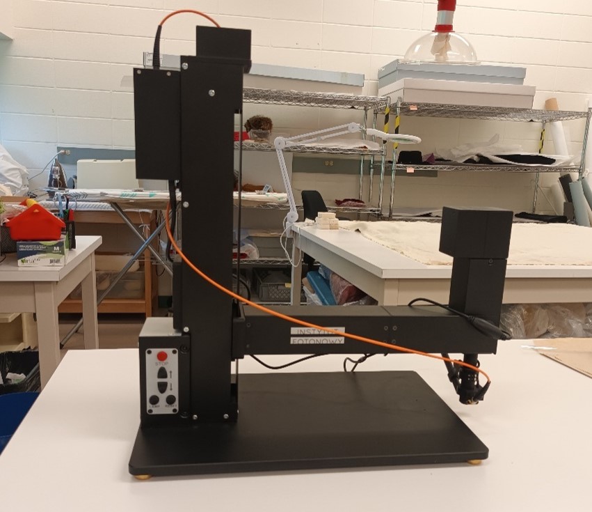 A black machine with a flat base plate and a square vertical column, about half a metre tall and wide. A horizontal arm extends from the column and is slightly longer than the base.