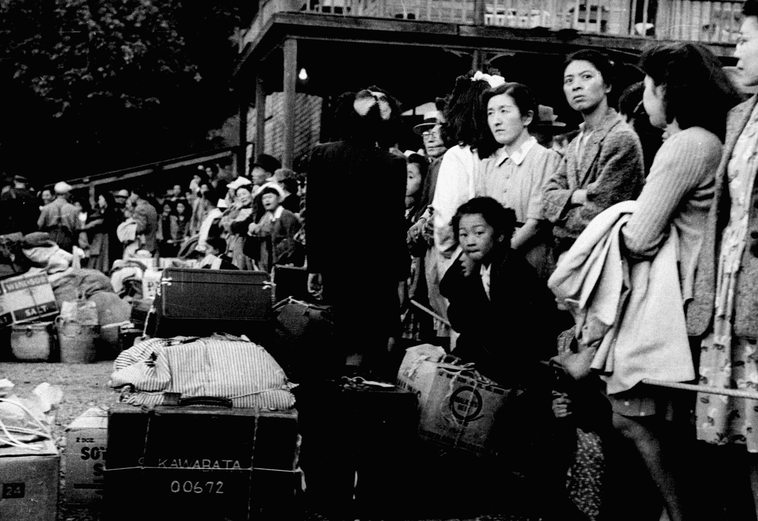 Photographie en noir et blanc de gens d’origine japonaise attendant un train.//Black-and-white photograph of Japanese Canadians waiting for a train.