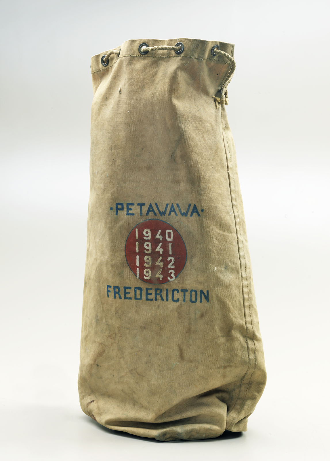 Sac de sport beige avec les mots Petawawa et Fredericton peints, et les dates de 1940 à 1943.//Beige duffle bag with painted words Petawawa and Fredericton, and the dates from 1940 to 1943.