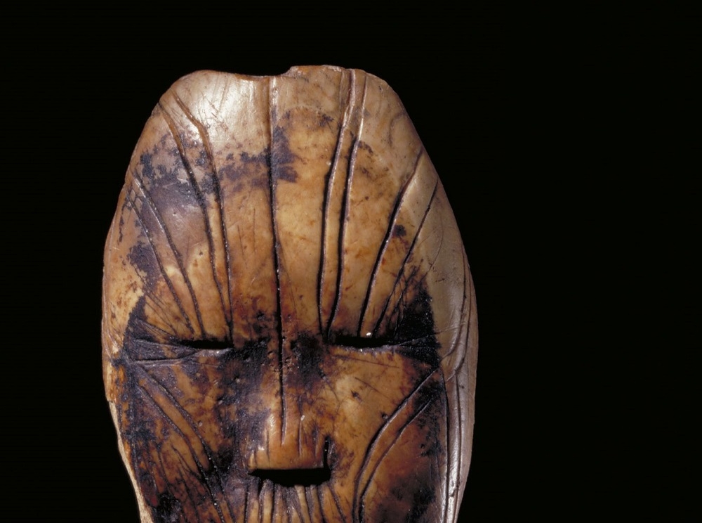 Small carving of a face with vertical lines running over it