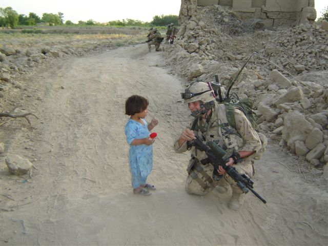 //A soldier kneels in front of a child holding a knitted doll