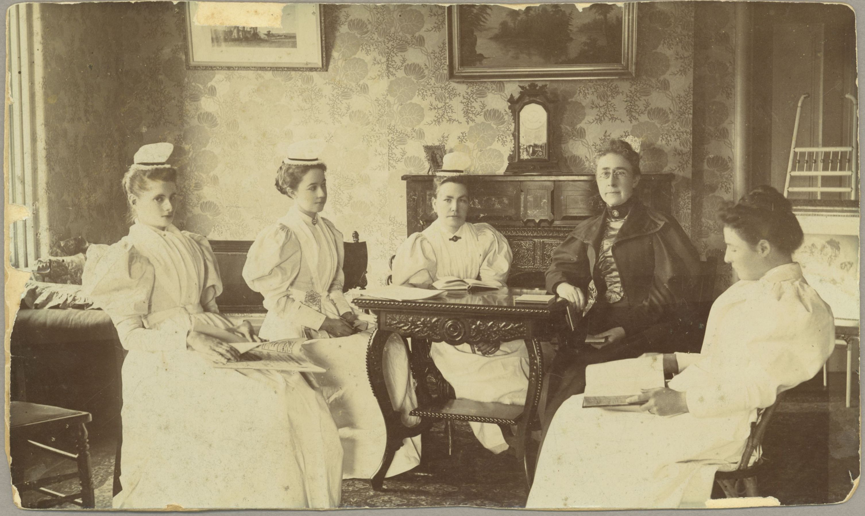 Nurses sitting at a table. Second woman on the left is wearing chatelaine. 