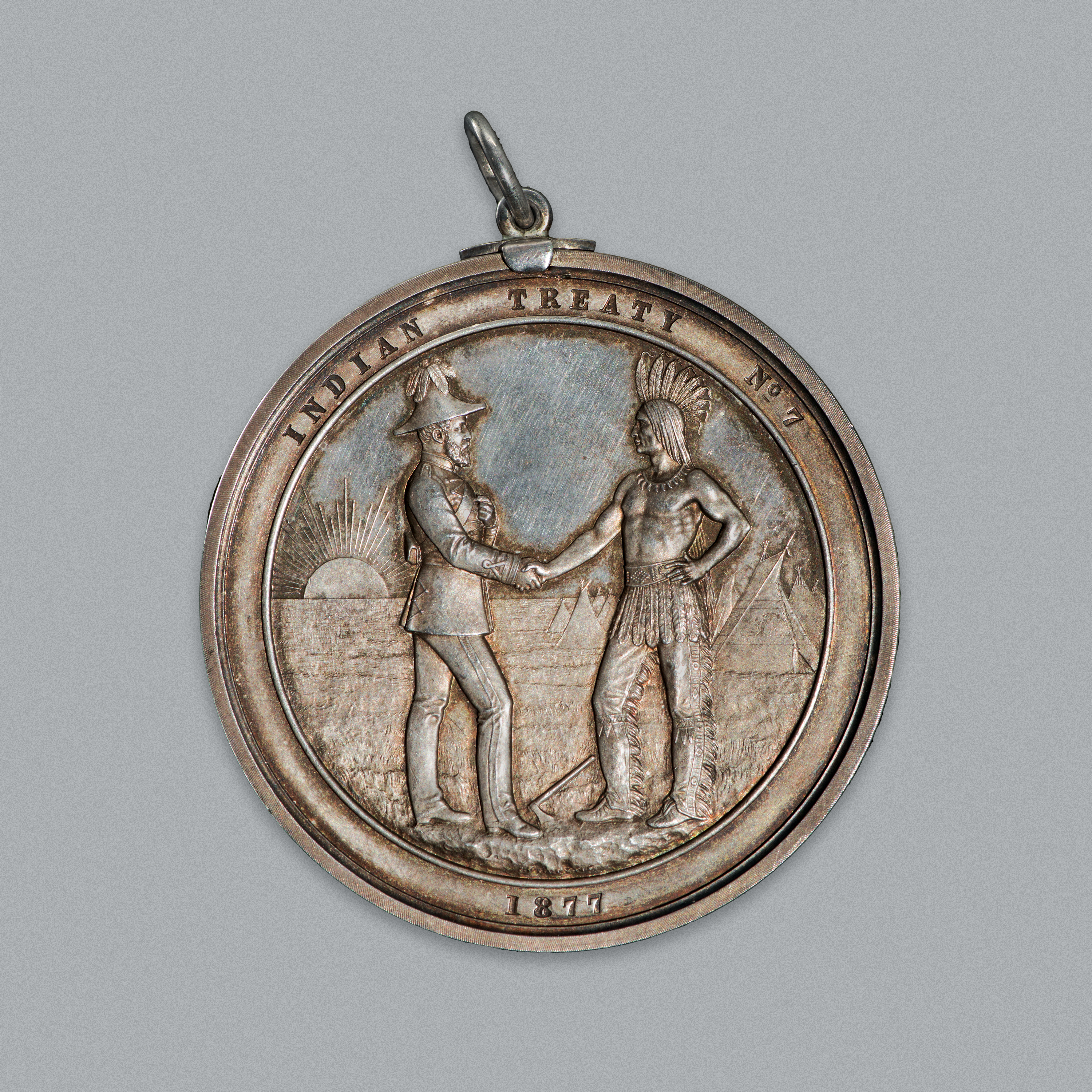 Médaille ronde en argent avec deux hommes, un Autochtone et un Britannique, se serrant la main. //Round silver medal with two men — one Indigenous, one British — shaking hands