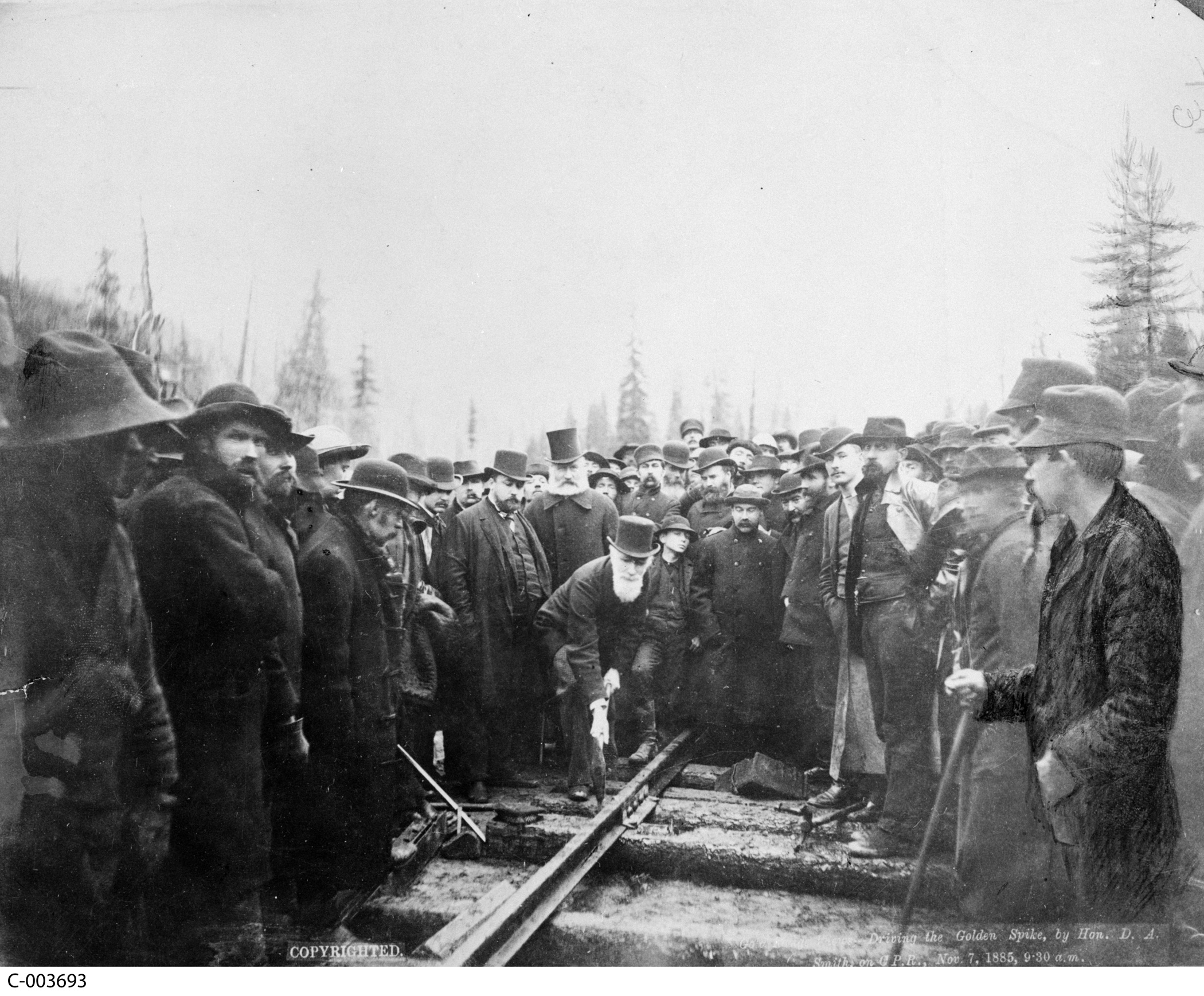 Groupe d’hommes autour d’un chemin de fer; l’un d’entre eux enfonce un crampon//Group of men around railway, one man drives a spike