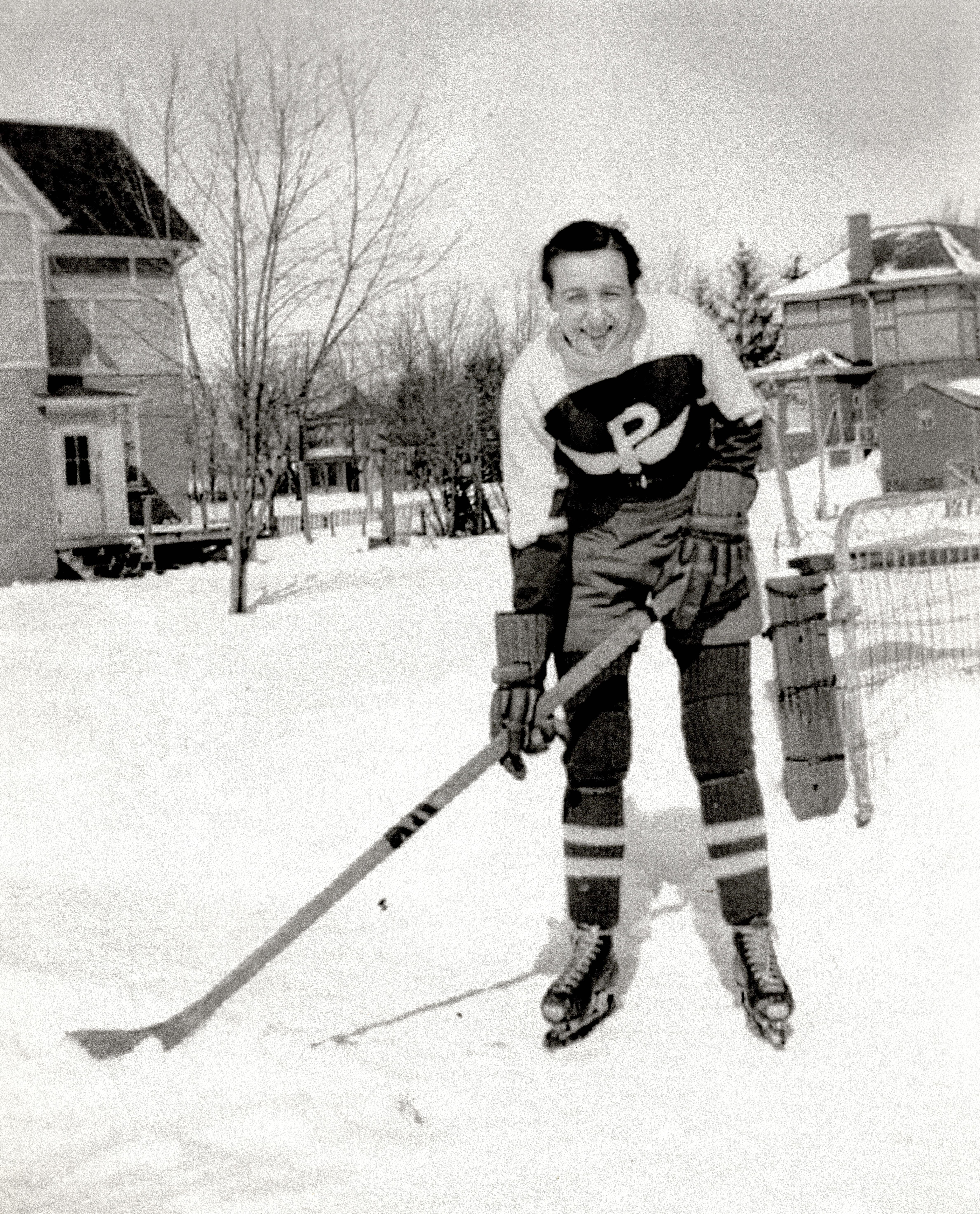 Photo en noir et blanc d’une femme portant de l’équipement de hockey sur une patinoire de jardin. //Black and white photo of a woman wearing hockey equipment on a backyard rink