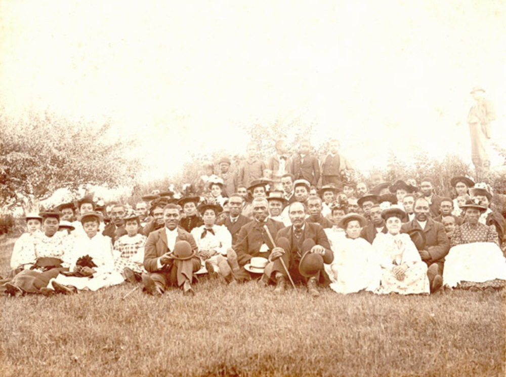 Sepia photograph showing church congregation dressed in their Sunday best. - Une photographie sépia montrant des membres d’une paroisse en habits du dimanche.