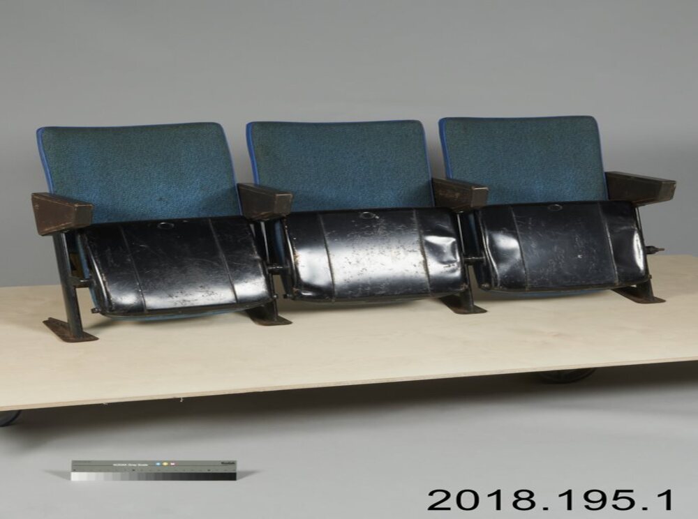 A row of three dark-blue theatre seats. - Une rangée de trois sièges de cinéma bleu foncé.