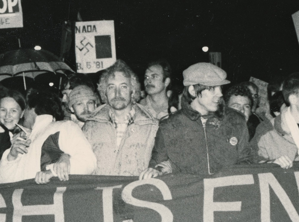 Zoom of a Black-and-white photograph of men with signs, behind a banner that reads, “Enough is Enough: Stop Police Violence.”