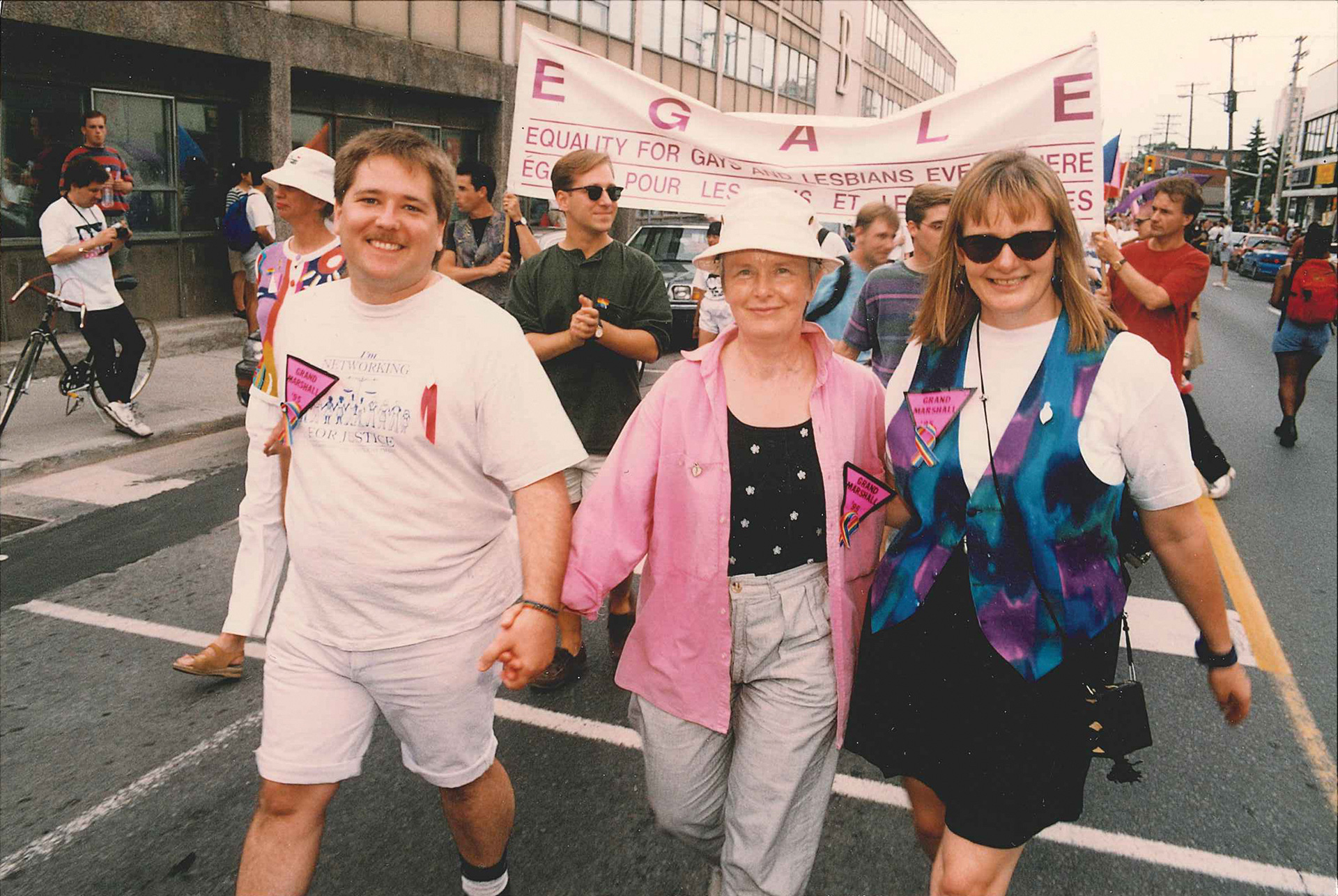 Trois femmes marchant ensemble dans la rue lors d’une parade de la Fierté Three women walking together down the street during a Pride parade.