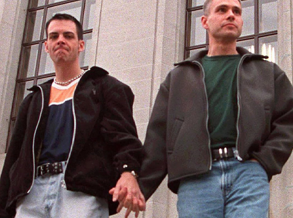 Deux jeunes hommes descendent des marches extérieures en se tenant par la main. Two young men walking down outdoor steps, holding hands.