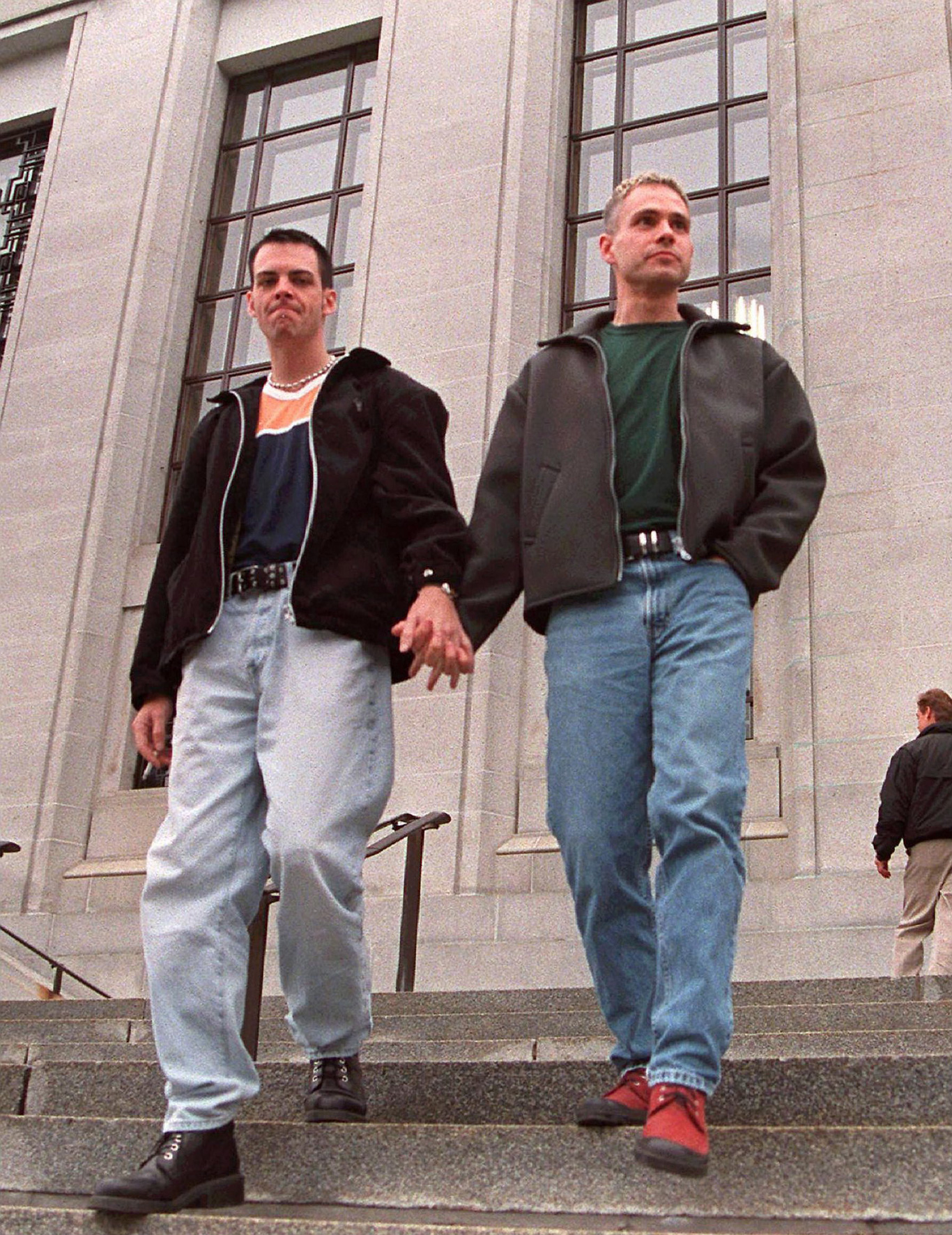 Deux jeunes hommes descendent des marches extérieures en se tenant par la main. Two young men walking down outdoor steps, holding hands.