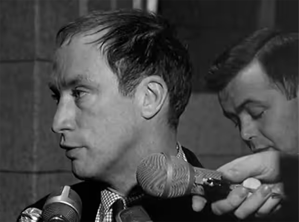 Photographie en noir et blanc de Pierre Trudeau s’adressant à des journalistes. Black-and-white photograph of Pierre Trudeau talking to reporters.