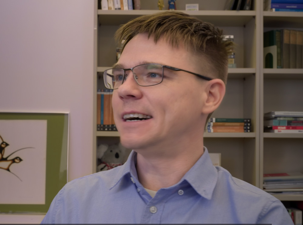 Capture d’écran de l’enregistrement vidéo mettant en scène Tom Hooper, un homme à lunettes habillé d’une chemise claire. Screenshot of a video clip featuring Dr. Tom Hooper, a man with glasses in a light-coloured shirt.