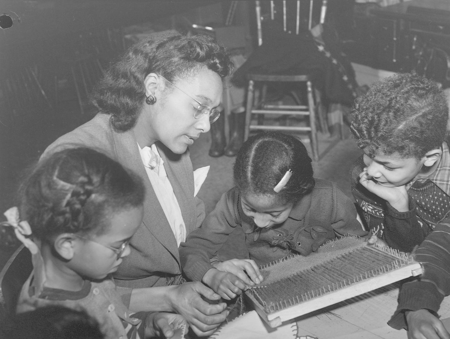 Photographie en noir et blanc d’une femme lisant un livre avec trois enfants.
