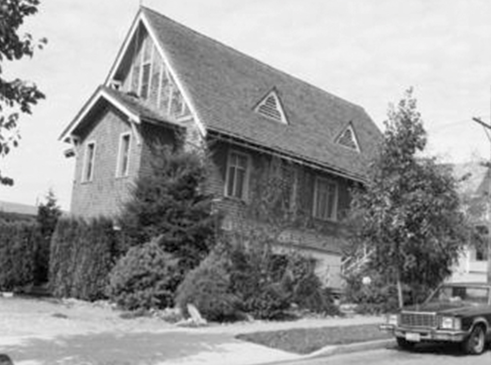 Photographie en noir et blanc d’une église avec une voiture garée devant.
