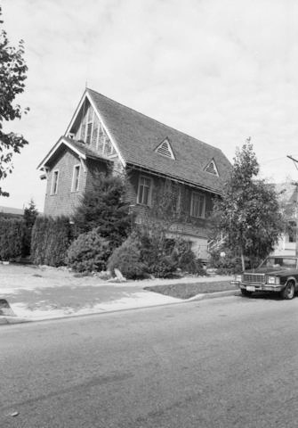 Photographie en noir et blanc d’une église avec une voiture garée devant.
