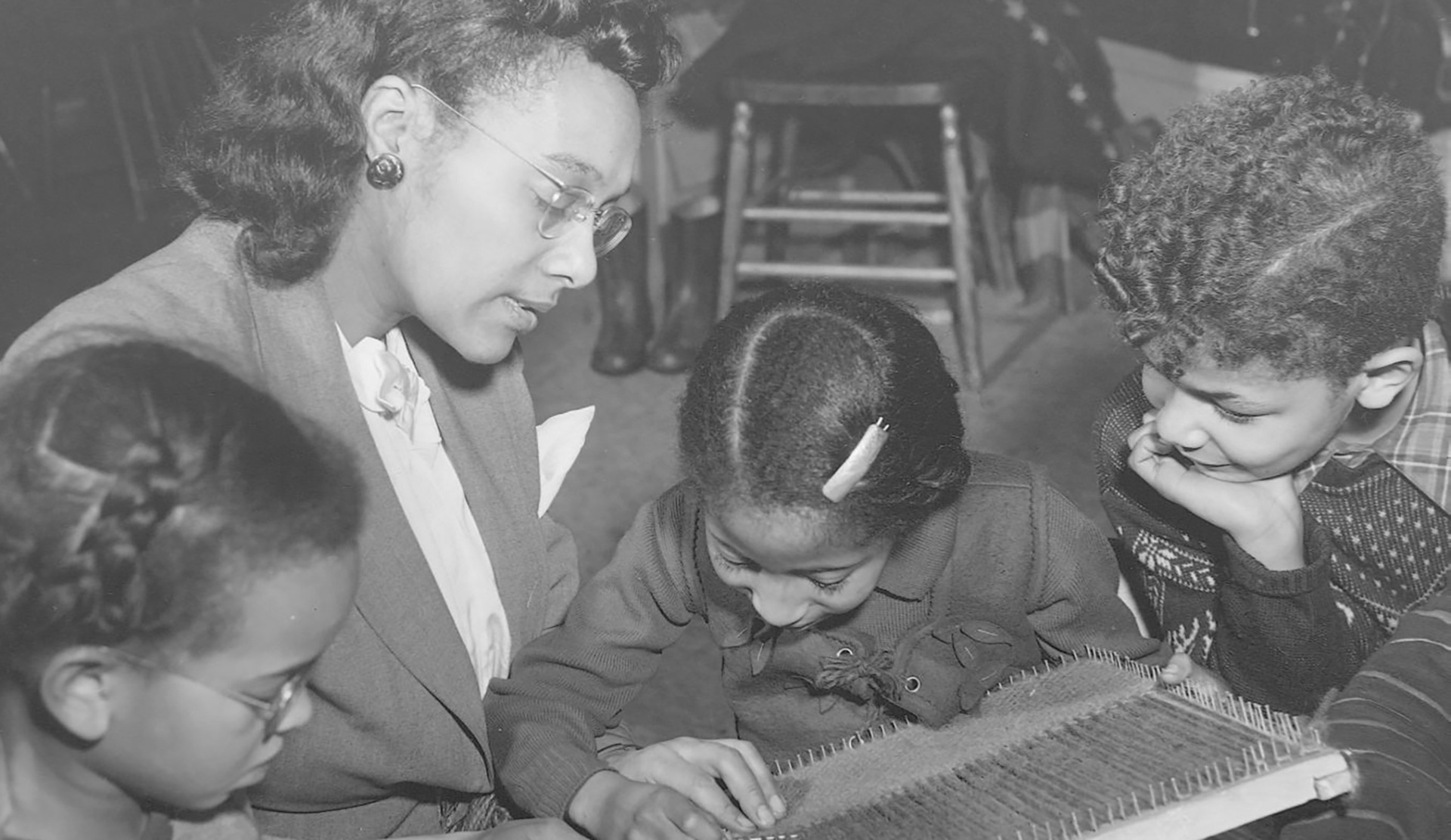 Photographie en noir et blanc d’une femme lisant un livre avec trois enfants.