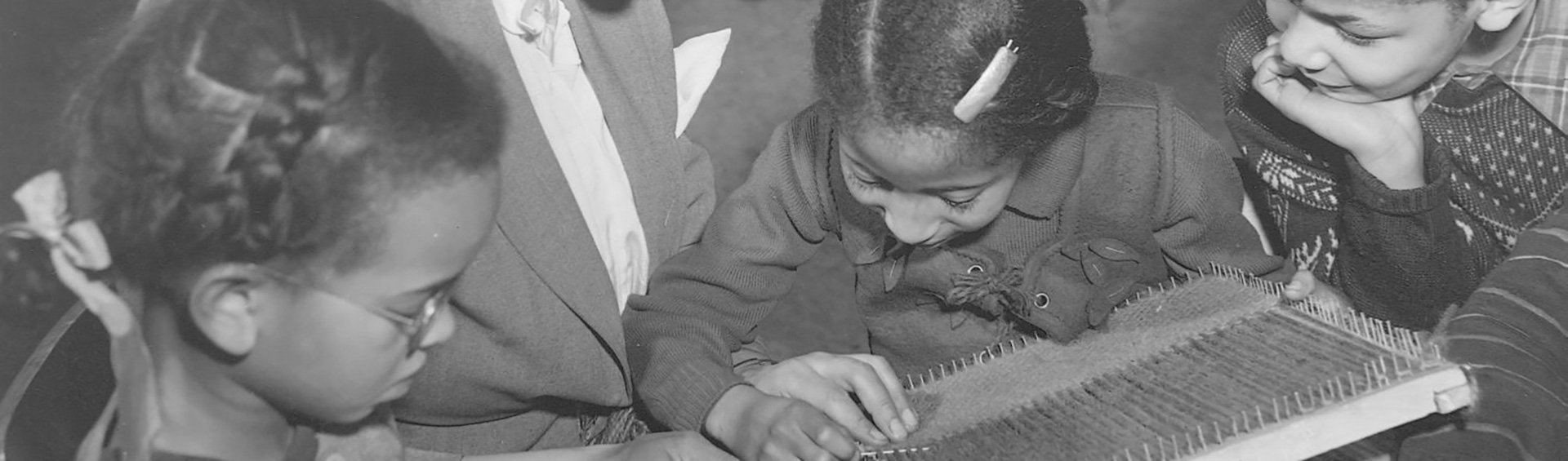 Photographie en noir et blanc d’une femme lisant un livre avec trois enfants.